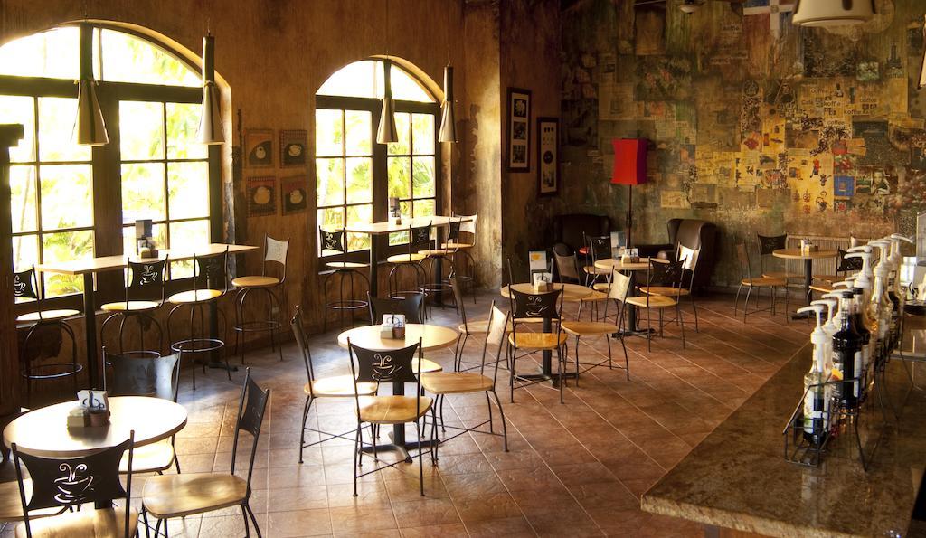Impressive Punta Cana Exterior foto The photo shows the interior of a café or restaurant. There are several small tables and chairs arranged throughout the space. Large windows allow natural light to fill the area, creating a warm atmosphere. The walls have a rustic, textured finish wi
